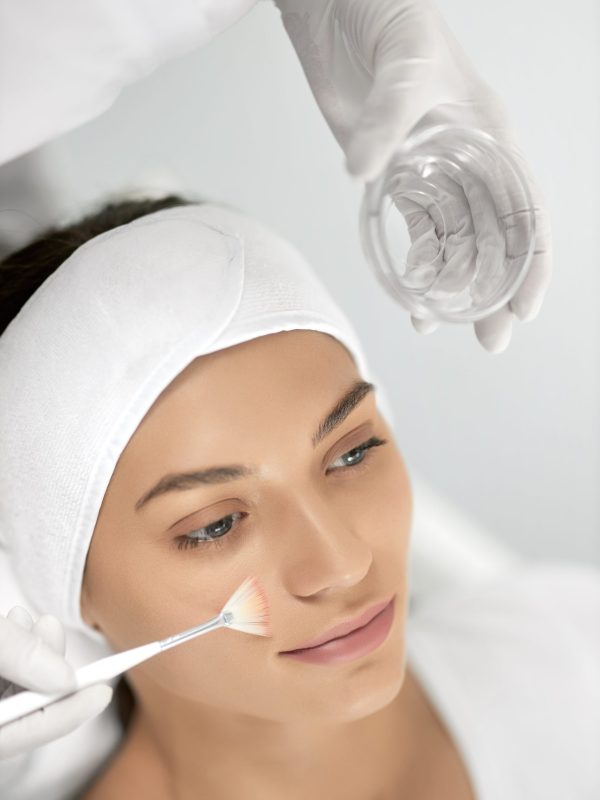 Top view portrait of beautician holding special masks for face and doing peeling for young beautiful woman. Concept of improvements skin with special cosmetic procedure in beauty salon.