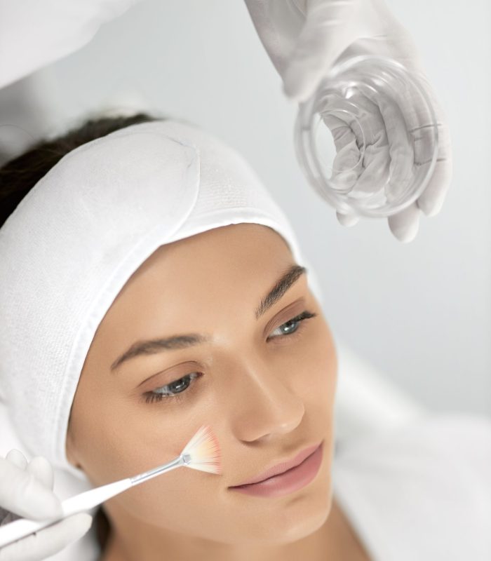 Top view portrait of beautician holding special masks for face and doing peeling for young beautiful woman. Concept of improvements skin with special cosmetic procedure in beauty salon.
